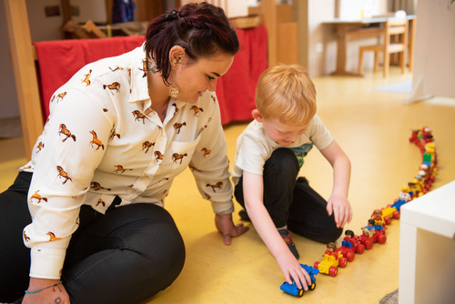 Kindergartenpädagogin sitzend am Boden betreut ein Kind